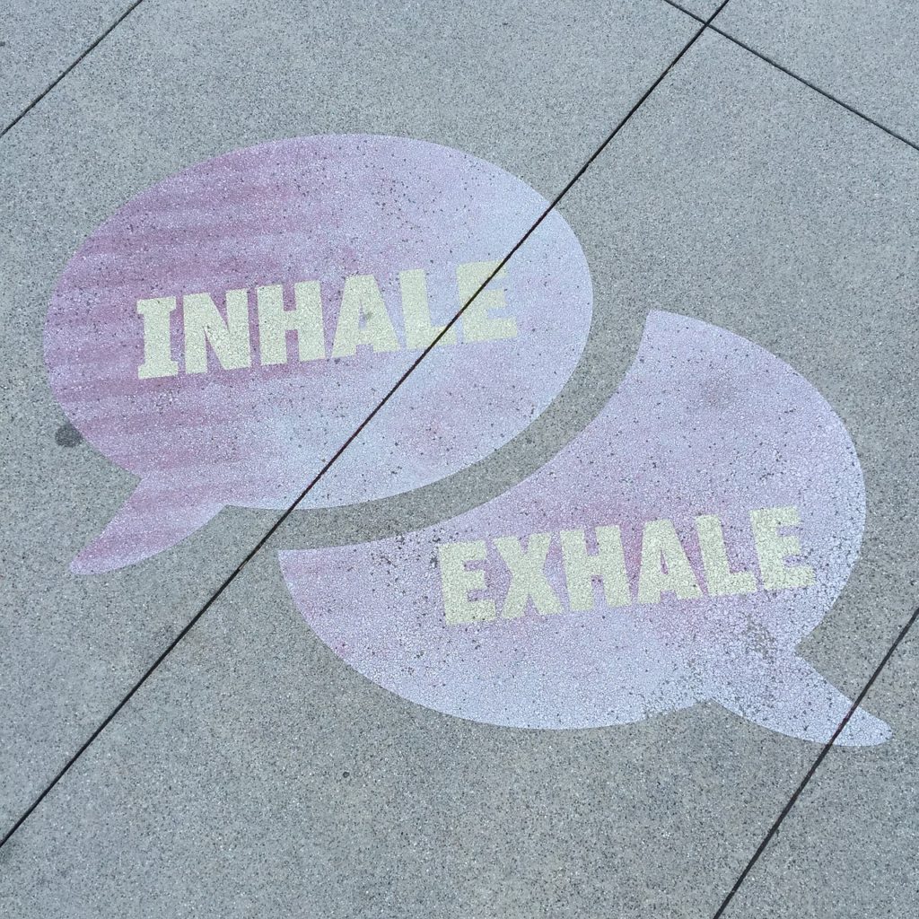 Purple comment bubbles painted on sidewalk with instructions to breathe. Top one reads "inhale" and cuts into bottom one which reads "exhale".