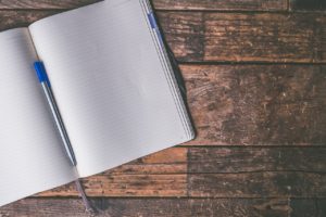 Close-up of open notebook with white lined pages and a pen in the fold on a brown wooden desk