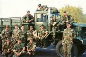 13 members of the military in camouflaged uniforms sitting on a military truck