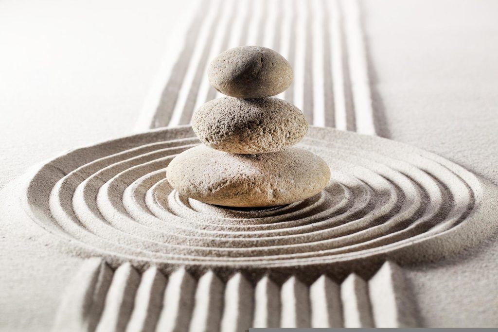 3 stones vertically balanced on a rings of sand