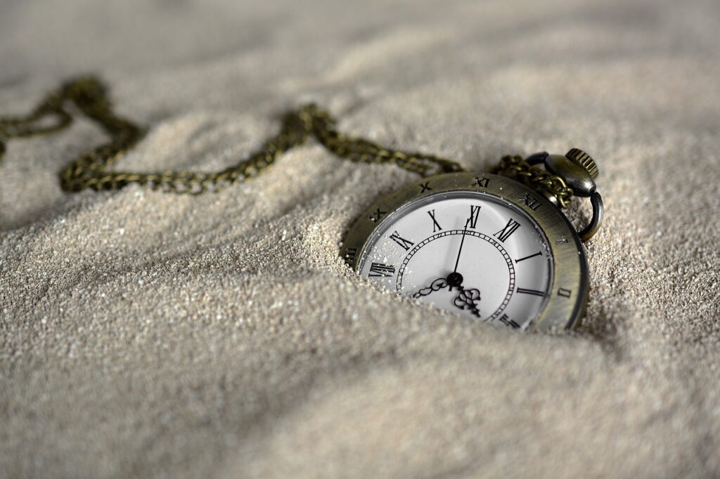 "An antique pocket watch partially buried in golden beach sand, its ornate metal casing and delicate hands contrasting with the textured grains of sand that surround it."