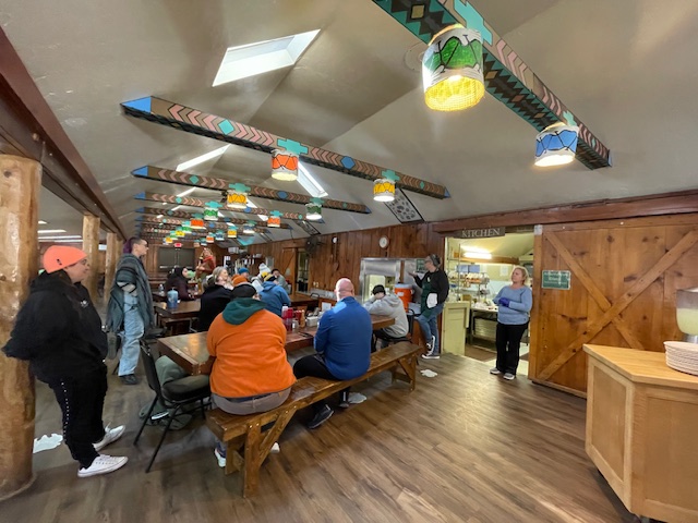 Adult campers sitting at wooden tables and benches in camp dining hall